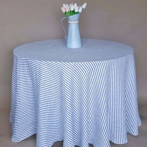 May include: A white tablecloth with blue diagonal stripes, featuring a blue metal pitcher with a bouquet of pink and white tulips.