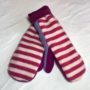 Op de afbeelding: Een paar roze en witte gestreepte wanten met paarse manchetten. De wanten zijn gemaakt van een zachte, gebreide stof.