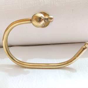 May include: A gold-colored, curved towel ring with a circular mounting plate and a ball-shaped finial. The ring has a smooth, polished finish and is designed for bathroom use.