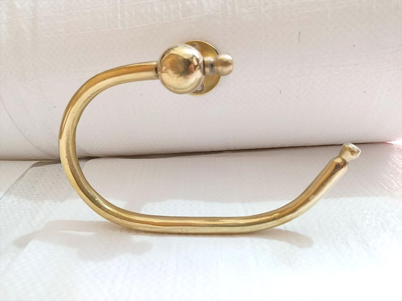 May include: A gold-colored, curved towel ring with a circular mounting plate and a ball-shaped finial. The ring has a smooth, polished finish and is designed for bathroom use.