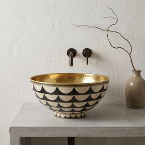May include: A round vessel sink featuring a hammered gold interior and an exterior decorated with a repeating black and cream scalloped pattern. The sink is paired with a dark bronze wall-mounted faucet and a single handle control lever.