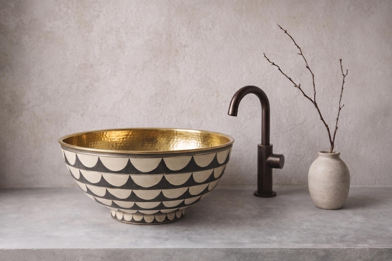May include: A round vessel sink featuring a hammered gold interior and an exterior decorated with a repeating black and white scalloped pattern. The sink is paired with a dark bronze gooseneck faucet and a small beige vase with a bare twig.
