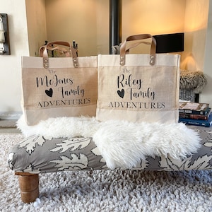 May include: Two brown burlap tote bags with leather handles. The bags have the text "The McJones Family Adventures" and "The Riley Family Adventures" printed on them.