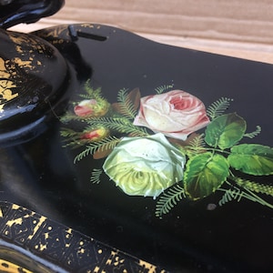 May include: Close-up of a black sewing machine with gold accents and a hand-painted floral design featuring white and pink roses with green leaves.
