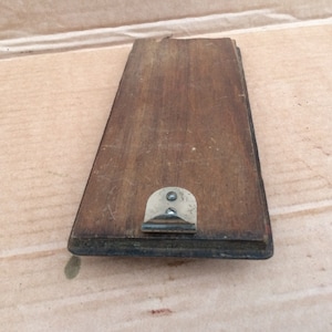 Pu&ograve; includere: Una cornice rettangolare in legno con un gancio di metallo sul retro. La cornice &egrave; di colore marrone scuro e ha una finitura usurata.