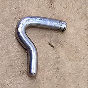 May include: A shiny, silver-colored metal hook with a curved shape. The hook has a smooth, reflective surface and is set against a textured, light brown background. The hook's design suggests it is for hanging or securing items.