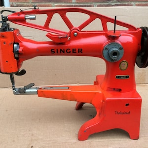 May include: A red Singer sewing machine with a metal frame and a foot pedal. The machine has a black belt and a label that says "Professional".