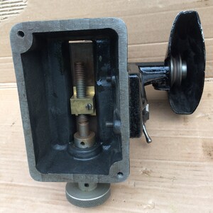 Puede incluir: Primer plano de una m&aacute;quina de metal negro con un tornillo de lat&oacute;n y una perilla negra. La m&aacute;quina tiene una base rectangular y una parte superior redonda. El tornillo es visible a trav&eacute;s de una abertura rectangular en la base.