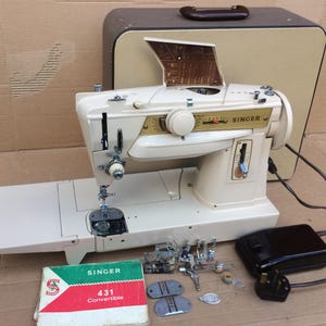 Könnte beinhalten: Eine vintage weiße Singer 431 Convertible Nähmaschine mit Tragetasche, Fußpedal und verschiedenen Zubehörteilen. Die Maschine verfügt über einen eingebauten Nadeleinfädler und eine einsetzbare Spule.