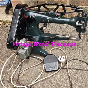 Pode incluir: Máquina de costura industrial vintage com acabamento em verde escuro e preto. A máquina tem um design mecânico complexo, com motor, pedal e várias alavancas e mostradores. Projetada para tarefas de costura pesadas.