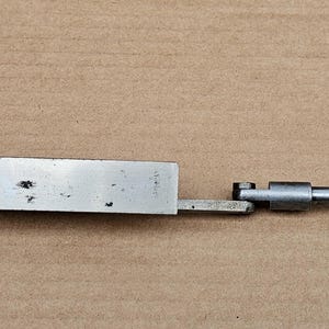 Może przedstawiać: Srebrne narzędzie mechaniczne z uchwytem w kształcie motyla i długim, prostym ramieniem. Narzędzie posiada szereg przegubów i prawokątny koniec. Tekst "22-23" jest widoczny na uchwycie. Narzędzie wydaje się służyć do pomiaru lub regulacji.