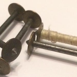 May include: Two antique wooden spools with metal axles and a single spool of white thread.