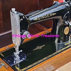 May include: A vintage black Singer sewing machine in a wooden case. The machine has a metal foot pedal and a needle plate with a decorative design. The case is made of wood with a dark stain.