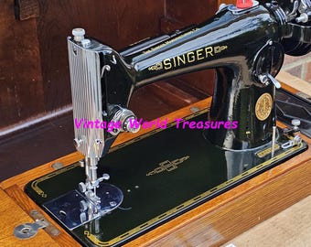 Puede incluir: Una máquina de coser Singer vintage negra en una caja de madera. La máquina tiene un pedal de metal y una placa de aguja con un diseño decorativo. La caja está hecha de madera con una mancha oscura.