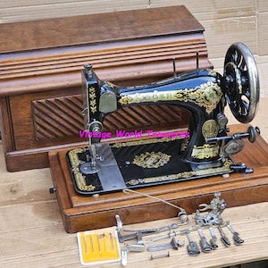 May include: Antique Singer sewing machine with a wooden case. The machine is black with gold accents and has a decorative design. The case is made of dark wood and has a hinged lid.