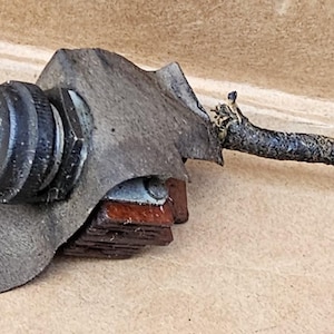 May include: A vintage toggle switch with a black ball-shaped knob and a metal base. The switch is mounted on a piece of worn leather and connected to a dark, curved wire. The item appears to be an electrical component.