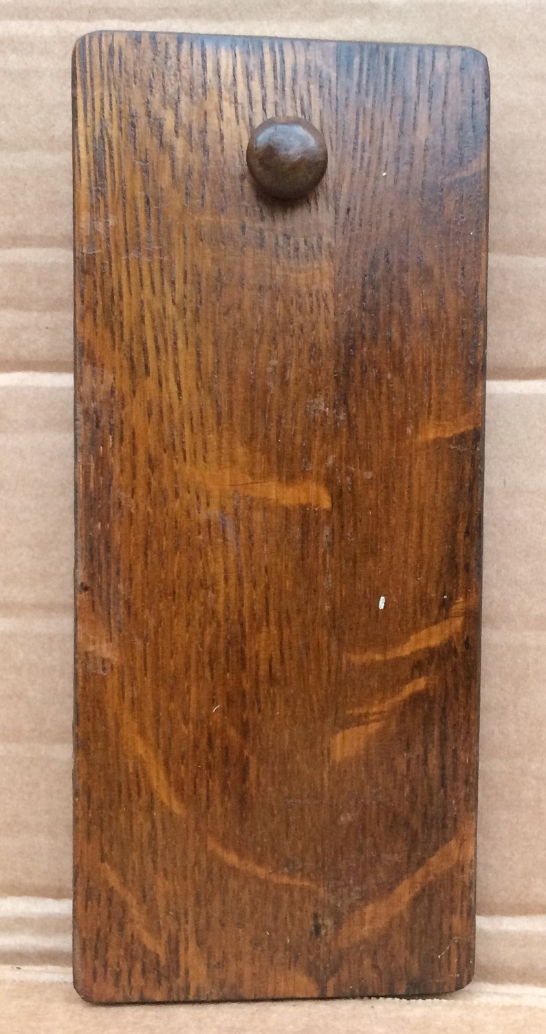 Pu&ograve; includere: Un cartello rettangolare in legno con una macchia marrone scuro. Il cartello ha un solo pomello rotondo al centro.
