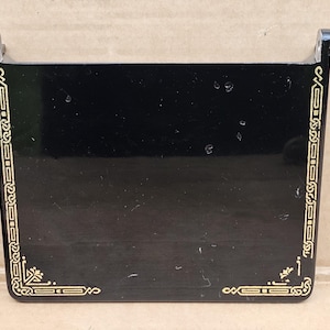 May include: Black sewing machine accessory with gold trim and a decorative pattern. The accessory is made of plastic and has a rectangular shape.