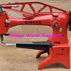 Pode incluir: Uma máquina de costura Singer vermelha com um pedal preto. A máquina tem uma bobina grande, redonda e metálica do lado direito. A máquina é etiquetada como "Singer" e "Profissional".