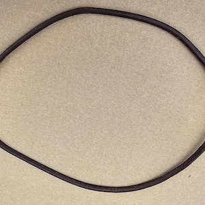 May include: A dark brown leather necklace, circular in shape, lies on a neutral background. The necklace appears to be made of a single, continuous piece of leather. The ends are joined with a small metal clasp.