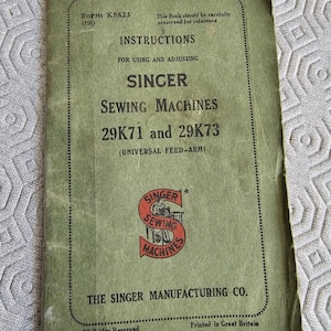 Peut inclure: Manuel d'instructions vert pour les machines à coudre Singer modèles 29K71 et 29K73. Le manuel porte le titre "Instructions pour l'utilisation et le réglage des machines à coudre Singer 29K71 et 29K73 (bras d'entraînement universel)". La couverture présente le logo Singer Sewing Machines avec un S rouge et une femme qui coud.