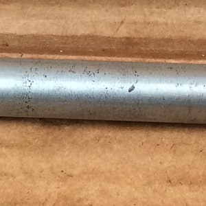 Op de afbeelding: Een zilveren metalen gereedschap met een handvat en een lang, cilindrisch lichaam. Het gereedschap heeft een reeks markeringen op het lichaam, waaronder nummers en lijnen.
