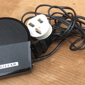 May include: Black foot pedal with a black cord and a white three-prong plug. The foot pedal has the word "RICCAR" printed on it.