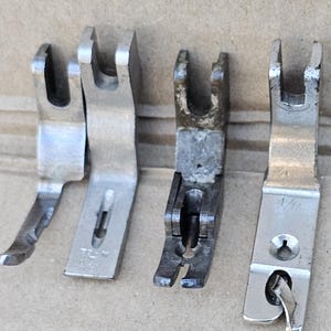 May include: Four vintage sewing machine presser feet. The feet are made of metal and have a variety of shapes and sizes. The feet are in various conditions, with some showing signs of wear and tear. The feet are designed to hold fabric in place while sewing.