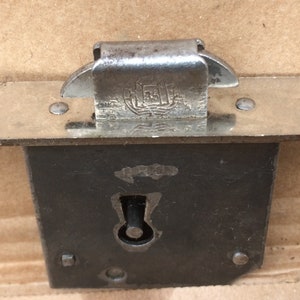 Peut inclure: Une serrure de porte en argent avec un trou de serrure et une poignée à levier en argent. Le loquet est monté sur une plaque métallique avec deux trous pour vis. La poignée à levier a une petite plaque métallique avec le texte "REGD" dessus.