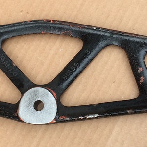 Puede incluir: Herramienta de metal negro con una palanca y un mango. La herramienta tiene una forma triangular con una abertura circular en el centro.