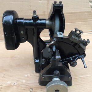 Puede incluir: M&aacute;quina de metal negro con una rueda de molienda y un brazo giratorio. La m&aacute;quina tiene un peque&ntilde;o motor y una manija para ajustar la rueda de molienda.