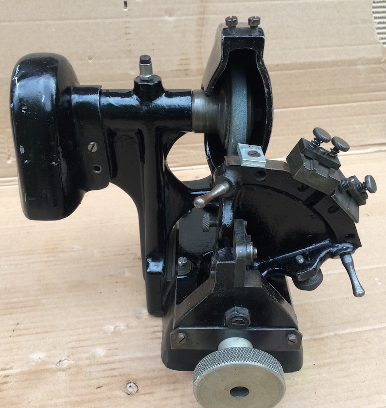 Puede incluir: M&aacute;quina de metal negro con una rueda de molienda y un brazo giratorio. La m&aacute;quina tiene un peque&ntilde;o motor y una manija para ajustar la rueda de molienda.