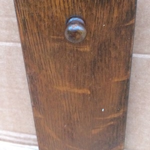 Pu&ograve; includere: Un fermaporta in legno marrone scuro con un pomo rotondo. Il fermaporta ha una venatura del legno naturale.