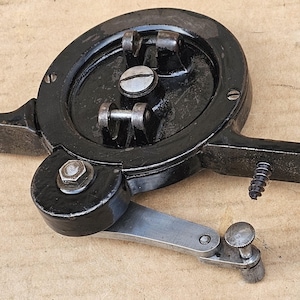 May include: Black metal tool with a round handle and a lever. The tool has a gear mechanism and several screws.