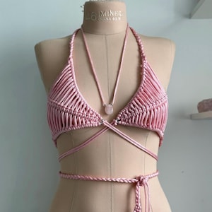 May include: A pink crocheted halter top with a pink stone pendant. The top is tied at the front and back with long straps.
