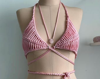 May include: A pink crocheted halter top with a pink stone pendant. The top is tied at the front and back with long straps.