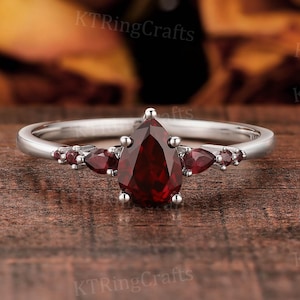 May include: A pear-shaped red gemstone ring with smaller red gemstones on the band. The ring is set in silver.