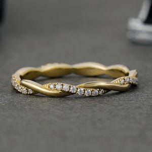 May include: A gold ring featuring a twisted band design. One strand of the band is polished gold, while the other strand is set with a row of small, clear, round-cut stones that sparkle along the front half of the circular jewelry piece.