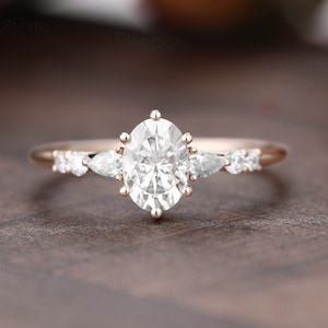 May include: A rose gold engagement ring featuring a large oval-shaped centre stone and smaller pear-shaped accent stones.