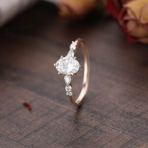 May include: A rose gold engagement ring with an oval-shaped center stone and smaller pear-shaped accent stones.