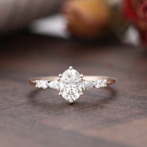 May include: A rose gold engagement ring with a large oval-shaped center stone and smaller pear-shaped accent stones.