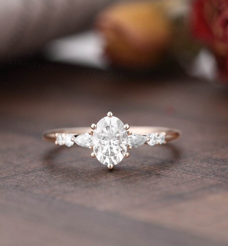 May include: A rose gold engagement ring with a large oval-shaped center stone and smaller pear-shaped accent stones.