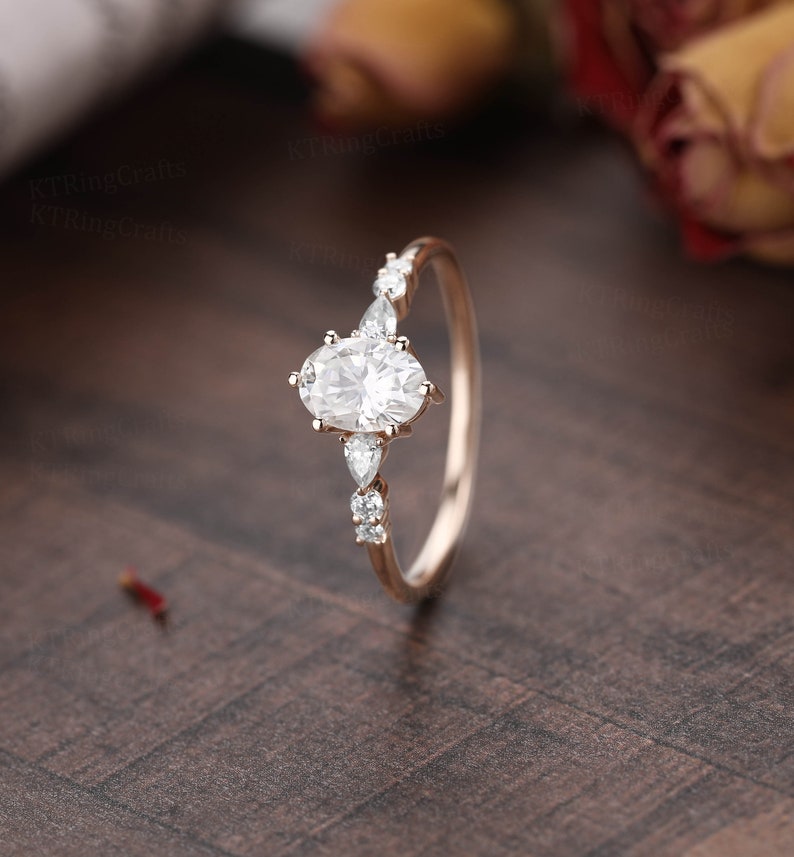 May include: A rose gold engagement ring with an oval-shaped center stone and smaller pear-shaped accent stones.