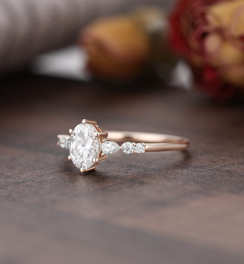 May include: A rose gold engagement ring with a large oval-shaped center stone and smaller pear-shaped accent stones.