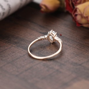 May include: A rose gold engagement ring with a large oval-shaped center stone and smaller accent stones on the band.