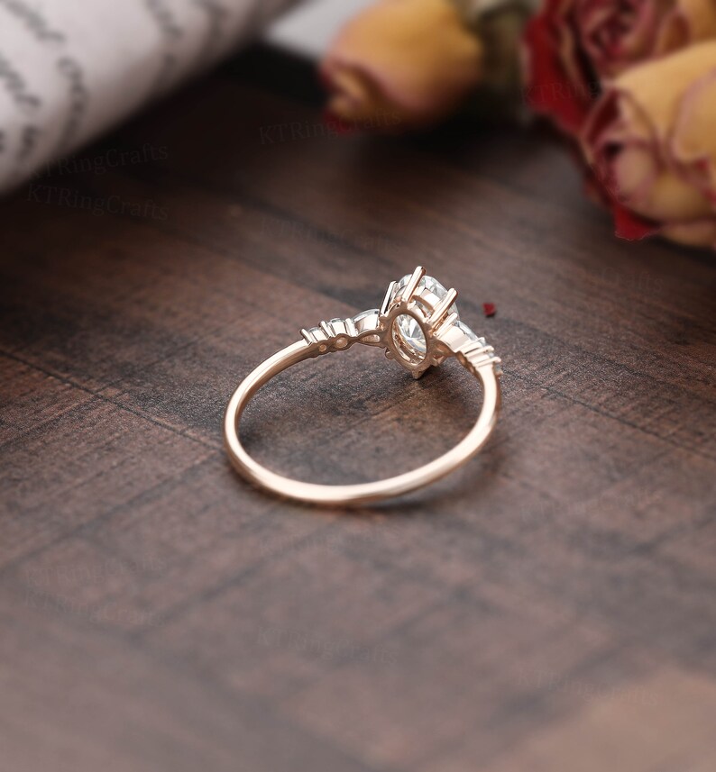 May include: A rose gold engagement ring with a large oval-shaped center stone and smaller accent stones on the band.