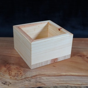 Peut inclure: Une boîte carrée en bois clair avec une finition naturelle. La boîte est vide et a une surface lisse.