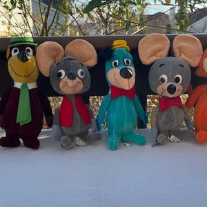 May include: A collection of six vintage plush cartoon character toys. The toys include a brown bear, a yellow-faced bear with a green hat, two gray mice, a blue dog, and an orange fox. Each character has a bow tie.