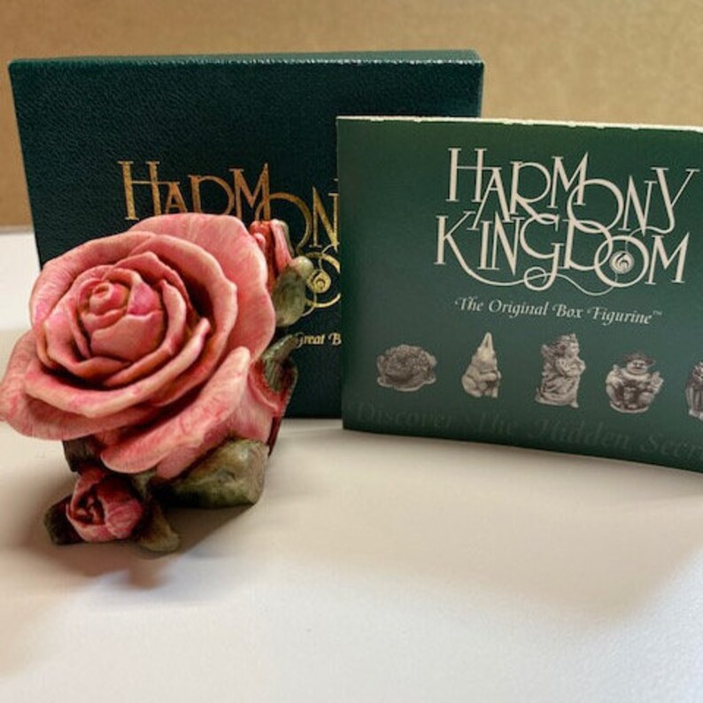 May include: A pink rose figurine with green leaves, part of the Harmony Kingdom "The Original Box Figurine" collection. The figurine is displayed on a green box with the Harmony Kingdom logo.