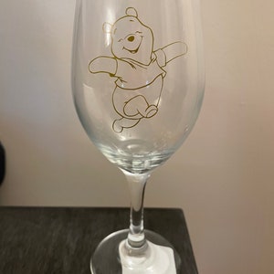 May include: A clear glass wine glass with a gold outline of Winnie the Pooh on the front.